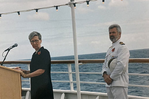 Joy standing at a podium as she gives a talk on the deck of a ship.